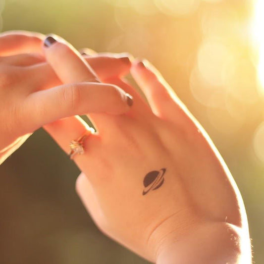 fake small little saturn minimalist temporary tattoo sticker design idea on wrist