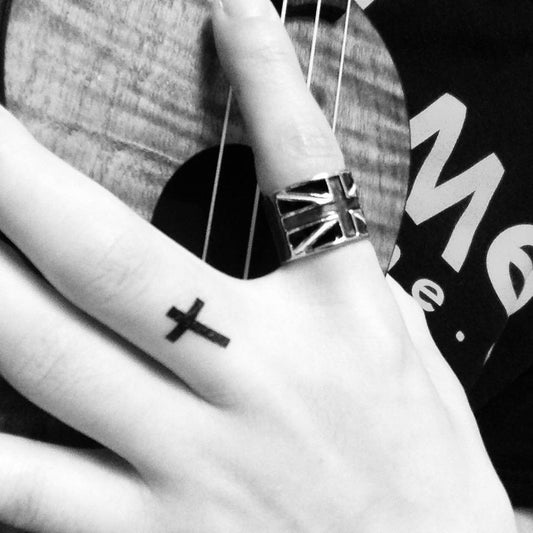 fake tiny little black cross on hand minimalist temporary tattoo sticker design idea on finger